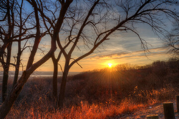 sunset sending rays across a leafless, winter forest with the Mississippi River in the distance, view from bluff, tree silhouettes framing a colorful sky, Pierre Marquet State Park Illinois