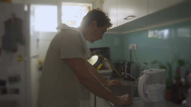 Sad, depressed, disappointed or tired young man stands in small kitchen at home