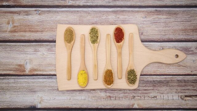 Spices in wooden spoons moving on cutting board on wooden table - Stop motion 