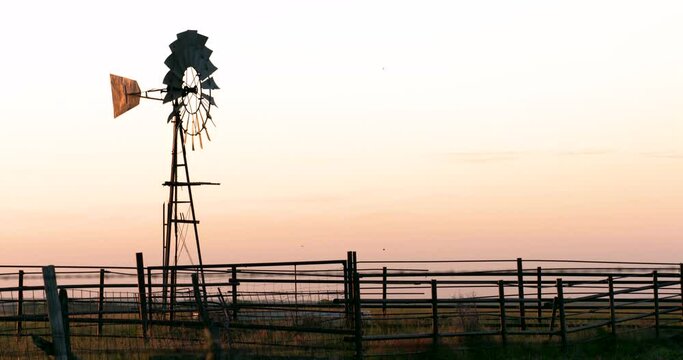 old windmill turning on prairie ranch pasture at sunset
