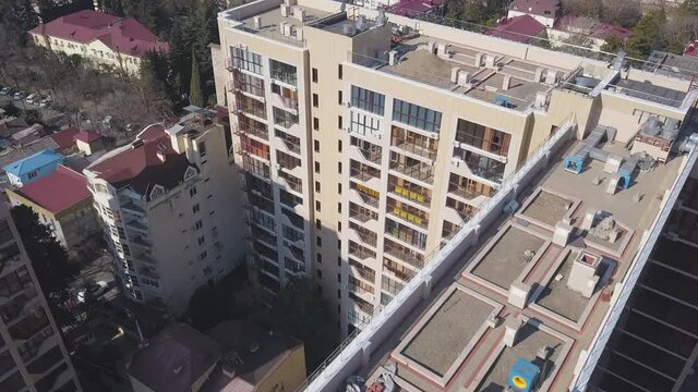 Aerial view of high rise residential building. Clip. Flying above the apartment house in the sleeping area of the city with parked cars on a summer sunny day.