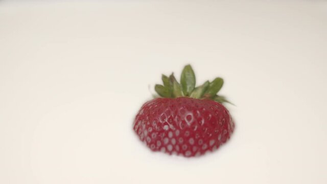 High quality close-up 4k slow motion video of a one strawberry falling into the vegan almond creamy coloured milk