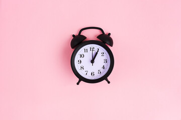View from above on black alarm clock on pink background. 1 p.m. Time is now