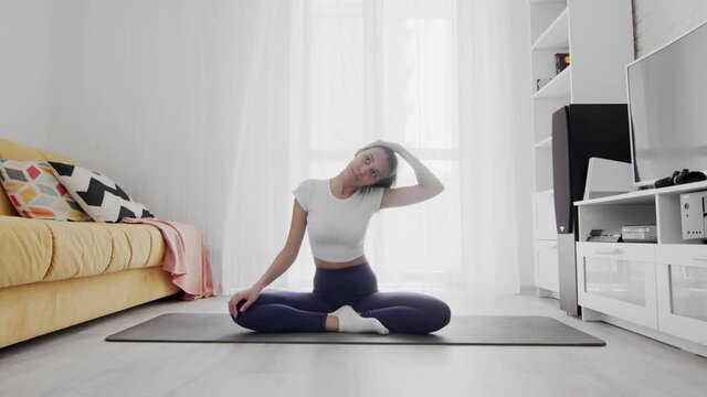 Young sporty african american woman stratching neck on mat at home