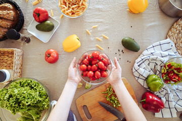 Hands holding plate with small tomatoes in kitchen. table with vegetables.