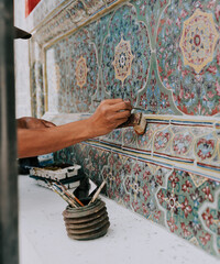 Man working and painting complicated mosaic in a wall from a temple in thailand