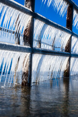 A frozen pier on the shore of the Baltic sea, large crystal clear icicles close-up. Bright blue...