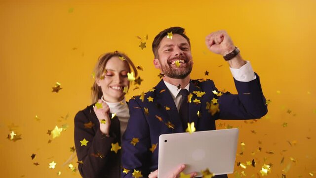 Business couple exults and celebrating success and victory. Isolated yellow background. Golden glitter falls