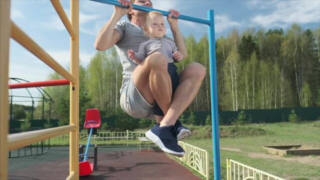 Family work out. Young man does pull ups with his baby. Adult male performs work out with his little child as additional weight.