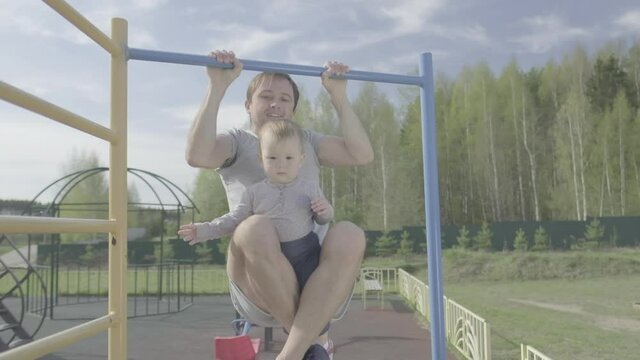 Family work out. Young man does pull ups with his baby. Adult male performs work out with his little child as additional weight. Flat log profile without color grading
