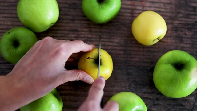 hand cutting apple into two halves on wooden table next to whole apples