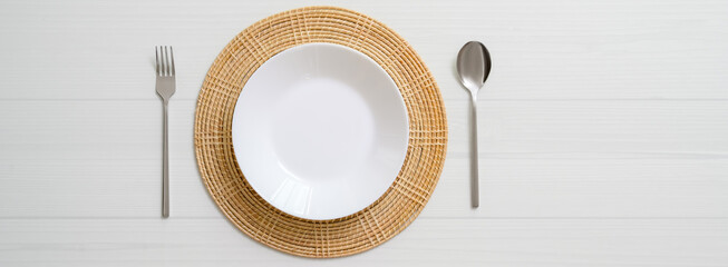 White plank dinning table with white ceramic plate on placemat and silverware