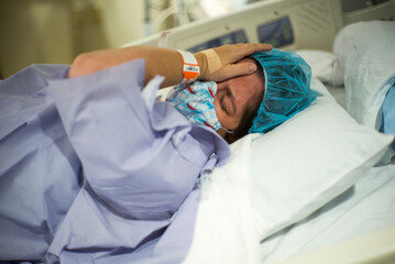 Pregnant woman in labor crying in hospital bed and wearing mask and PPE during Covid-19 pandemic waiting on birth or C-section delivery