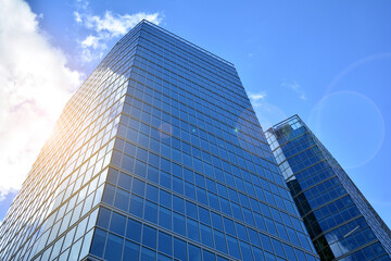 Fototapeta premium Facade texture of a glass mirrored office building. Fragment of the facade. Bottom view of modern skyscrapers in business district in evening light at sunset with lens flare filter effect.