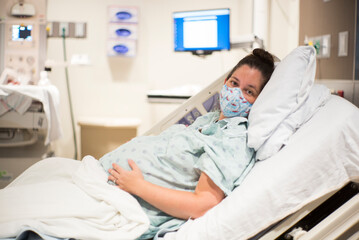 Pregnant woman about to deliver baby starting labor wearing mask isolated in maternity ward of hospital during Covid-19 Pandemic