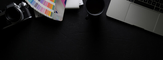 Dark modern designer workspace with laptop, camera, designer supplies, coffee cup and copy space