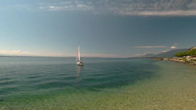 Lonely sail boat sailing out of a bay on a sunny day with blue water