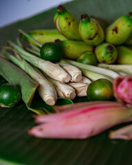 Asian food ingredients such as lemongrass, calamansi, tumeric leaves, torch lily and bananas on a banana leaf background.