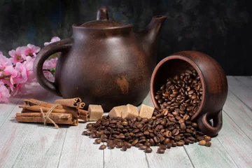 Foto op Aluminium an inverted mug with coffee beans on the background of a clay teapot, sugar cubes,cinnamon sticks and cherry blossoms on a wooden table © Владимир Олейник