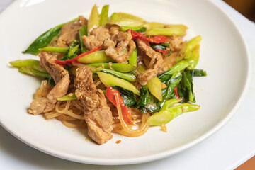 Stir-fried rice stick noodles in sweet soy sauce with pork, chili and chinese broccoli in white plate.