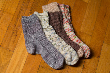 Hand knit socks, all different, laying on a hard wood floor.  Variety of socks in different colors and patterns, hand knit wool blends, isolated up close.