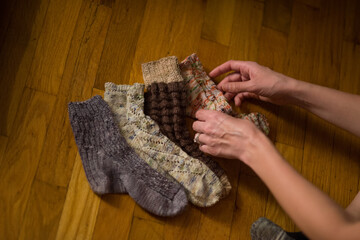 A woman arranges hand made knit socks on a hard wood floor.  At home crafts being arranged for a social media post.