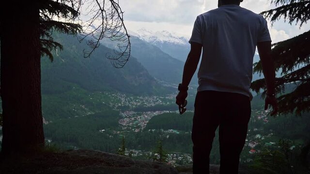 Wide angle shot of a man walking towards the cliff overlooking manali town in himachal pradesh