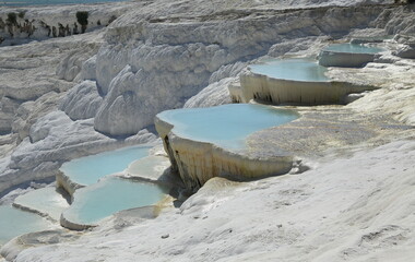 Pamukkale, Turkey. This region is a touristic city famous for its travertine formed by leaving white residue on the rock structure due to the water coming out of the rich carbonated water source.