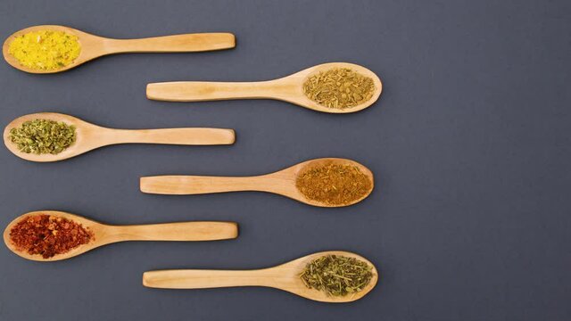 Wooden spoons with spices appear on grey background - Stop motion