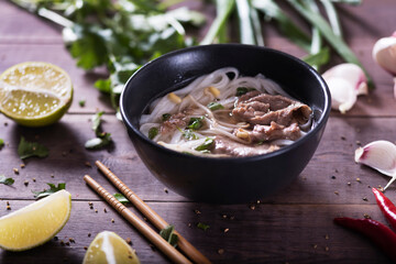 Asian cuisine, Vietnamese pho bo soup in a black plate on a wooden background