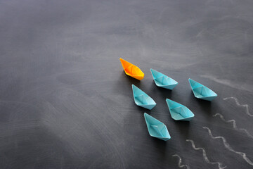 Leadership banner concept with paper boat on blackboard background. One leader ship leads others