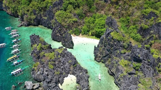 Hidden Beach, El Nido, Palawan Island, Philippines. Drone Aerial View of White Sand Lagoon Between Limestone Hills and Traditional Double Outrigger Boats on Coast