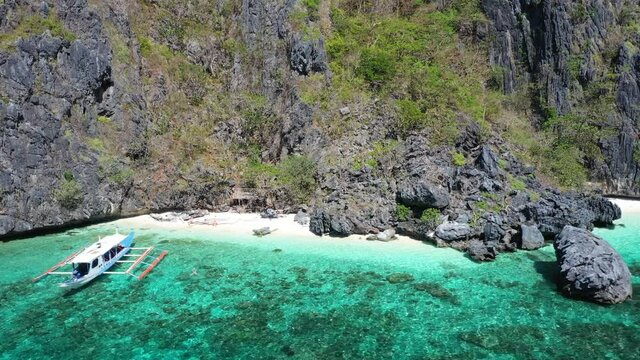 El Nido, Palawan Island, Philippines, Aerial View of Scenic White Sand Beach Under Steep Cliffs and Anchored Traditional Double Outrigger Boat
