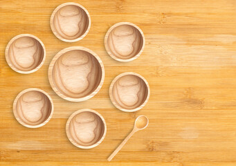 Top view big wooden empty bowl which surrounded by 6 small bowls, spoon aside on wooden table. Flat lay design template wooden 1 big bowl, 6 small bowls and 1 spoon, space for text and design.