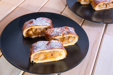Apple strudel on black plates on a wooden table, close-up, side view