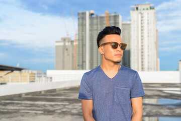 Young handsome multi ethnic man thinking with sunglasses against view of the city