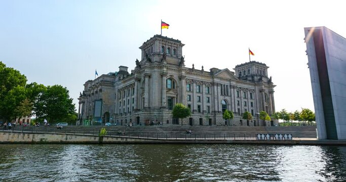 The German parliament, the Bundestag, in the Reichstag building at the city of Berlin. Hyper lapse on a sunny summer day at the river spree behind the building. The German national flag waving in the 