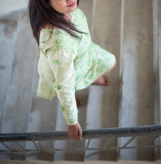 half face portrait of an Indian Bengali beautiful and cute brunette lady in a green casual dress climbing up a stair case while looking with happy smile. Indian lifestyle and fashion portrait.