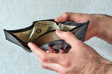 Hands of a man holding an open wallet in which one dollar lies