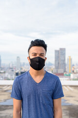 Face of young multi ethnic man wearing mask against view of the city