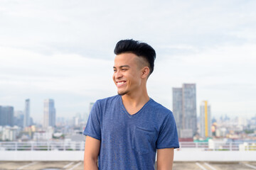 Happy young handsome multi ethnic man thinking against view of the city
