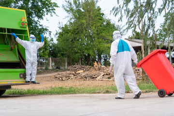 Worker in hazmat PPE protective clothing wearing protective mask to Protect Against Covid-19 are loading waste with garbage collector truck.