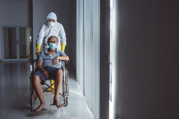 Medical worker in protective suit pushing aged man