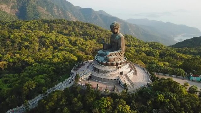 Aerial panning shot of people at Buddha statue amidst trees against sea, drone flying over famous monument - Hong Kong, China