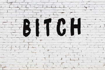 Word bitch painted on white brick wall