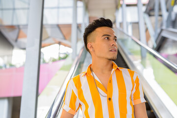 Young handsome multi ethnic man thinking while moving down the escalator in the city