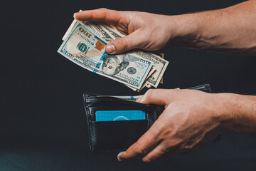Man on black background holds in his hands a wallet with dollars close up.