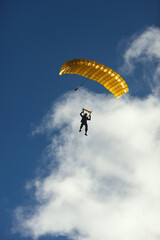 Skydiver silhouette under a bright yellow parachute canopy against the background of blue sky with clouds. Skydiving.