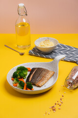 Fried salmon steak garnished with pepper, salt, olive oil, carrot, broccoli and mashed potatoes for healthy dinner on yellow background 