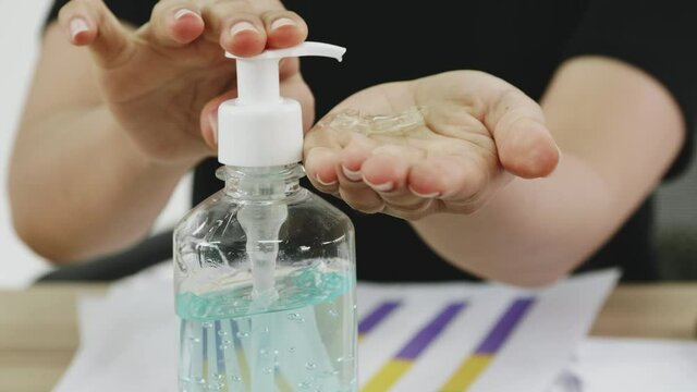 Business woman cleaning hands with sanitizer alcohol gel while working on her desk